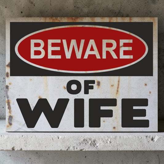 Rust-covered sign with 'Beware of Wife' text on a concrete wall.