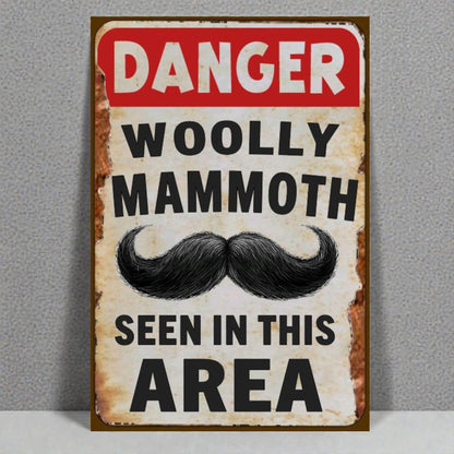 Vintage-style sign with a mustache graphic and text 'Danger Woolly Mammoth Seen in This Area' on a gray background.