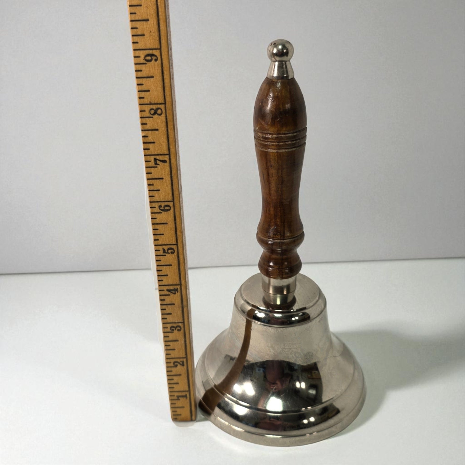 Silver bell with wooden handle next to a ruler on a white background