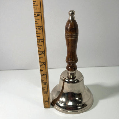 Silver bell with wooden handle next to a ruler on a white background