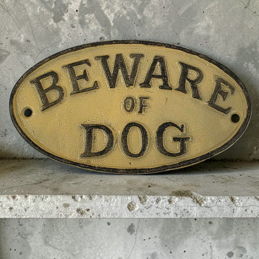 Oval metal sign with 'Beware of Dog' text on a concrete surface