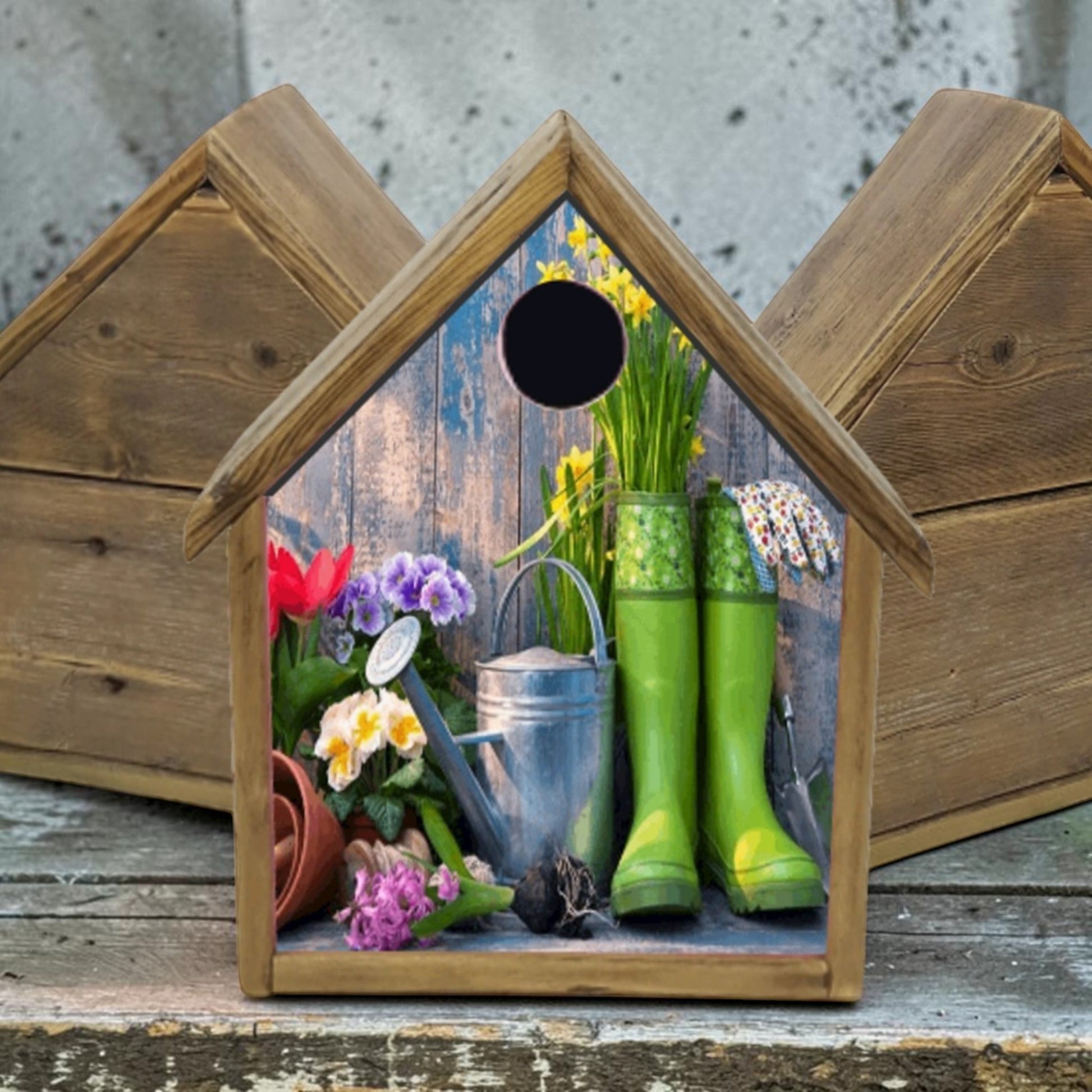 Wooden birdhouse with garden-themed decoration including green boots, flowers, and tools.