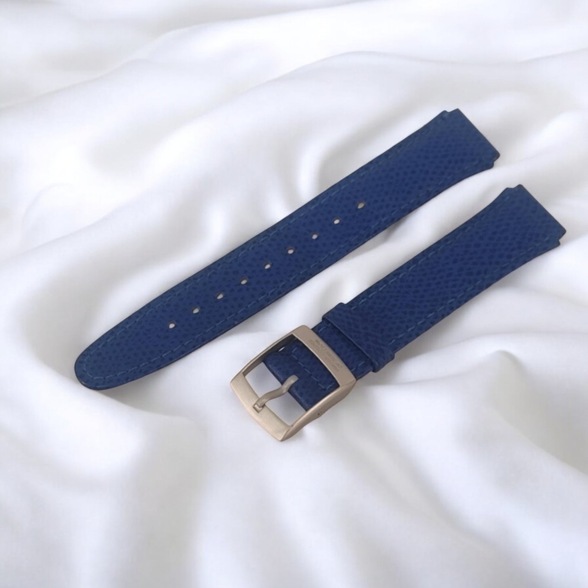 Blue watch strap with silver buckle on a white fabric background