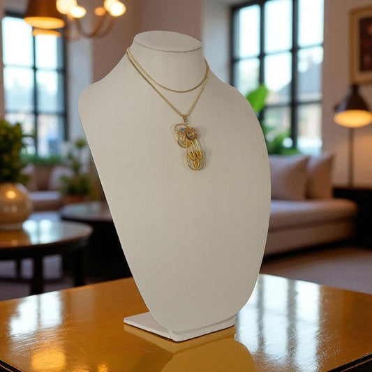 Mannequin bust with a gold necklace on a table in a room with large windows.