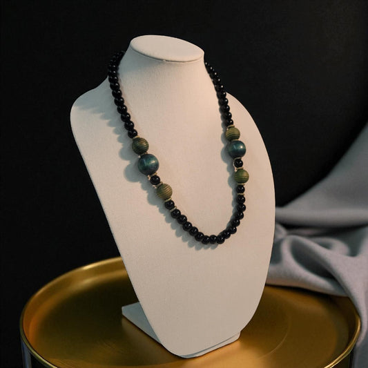 Necklace with black and green beads on a white mannequin bust against a dark background.