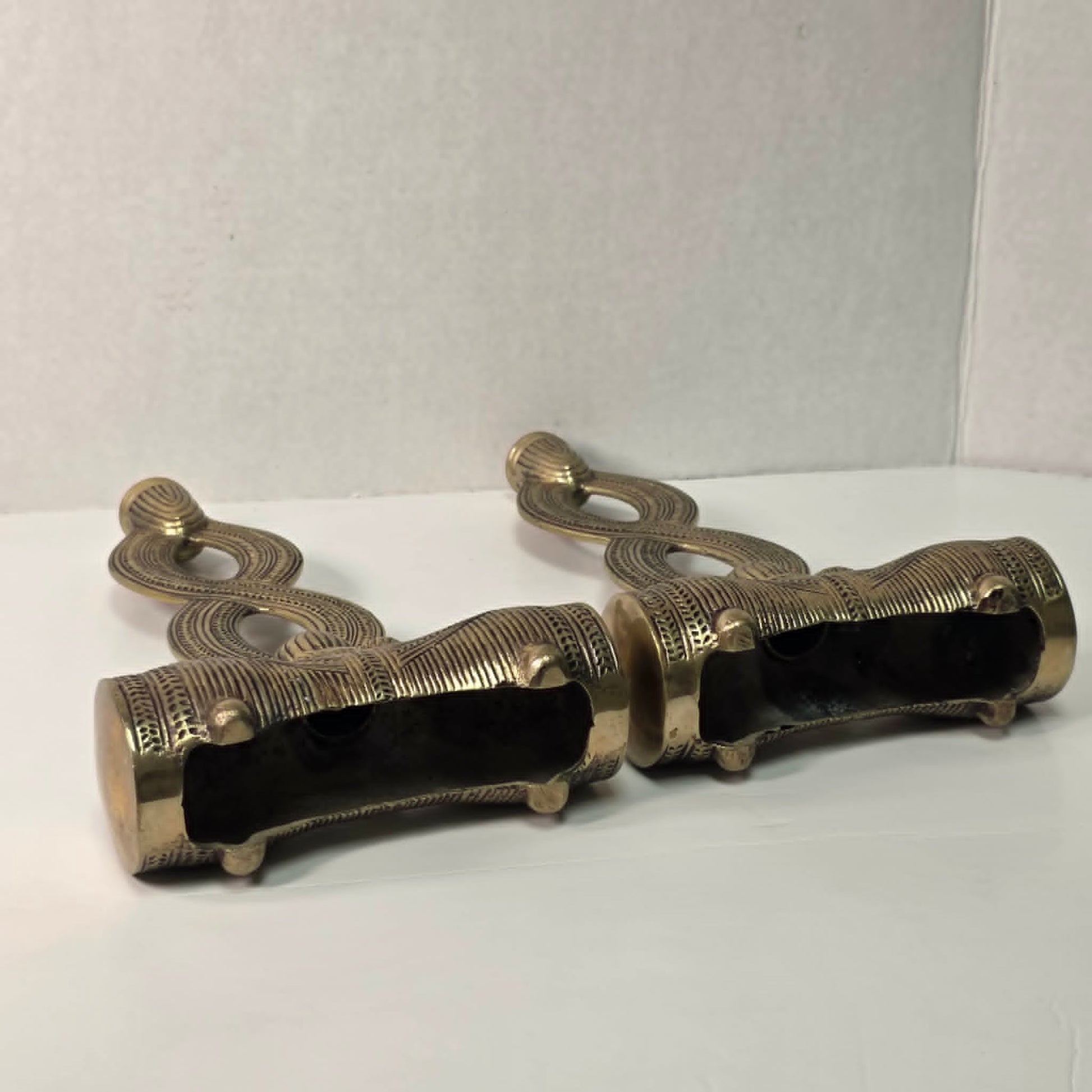 Pair of brass figure-eight candle holders with Egyptian-style engraved detailing.