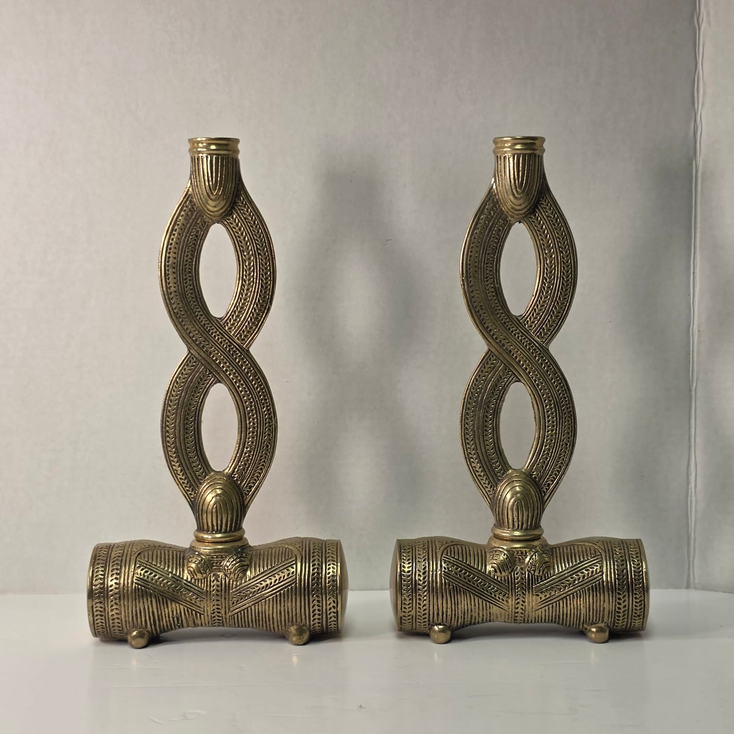 Pair of brass figure-eight candle holders with Egyptian-style engraved detailing.