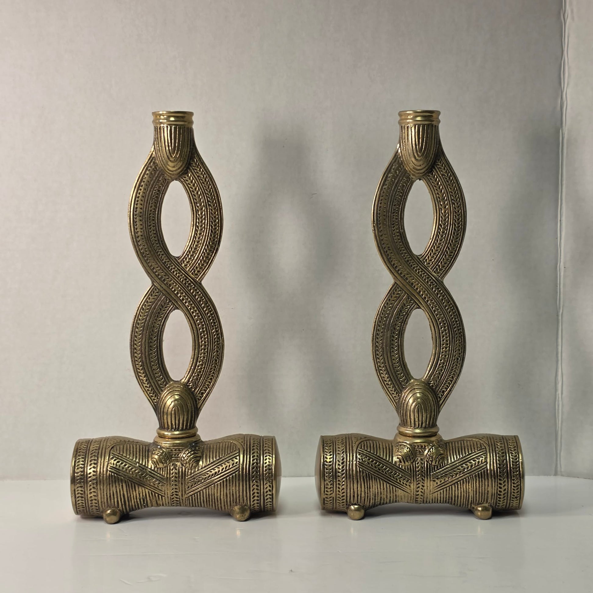 Pair of brass figure-eight candle holders with Egyptian-style engraved detailing.