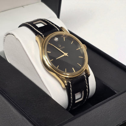 Gold wristwatch with black leather strap on a white cushion in a box