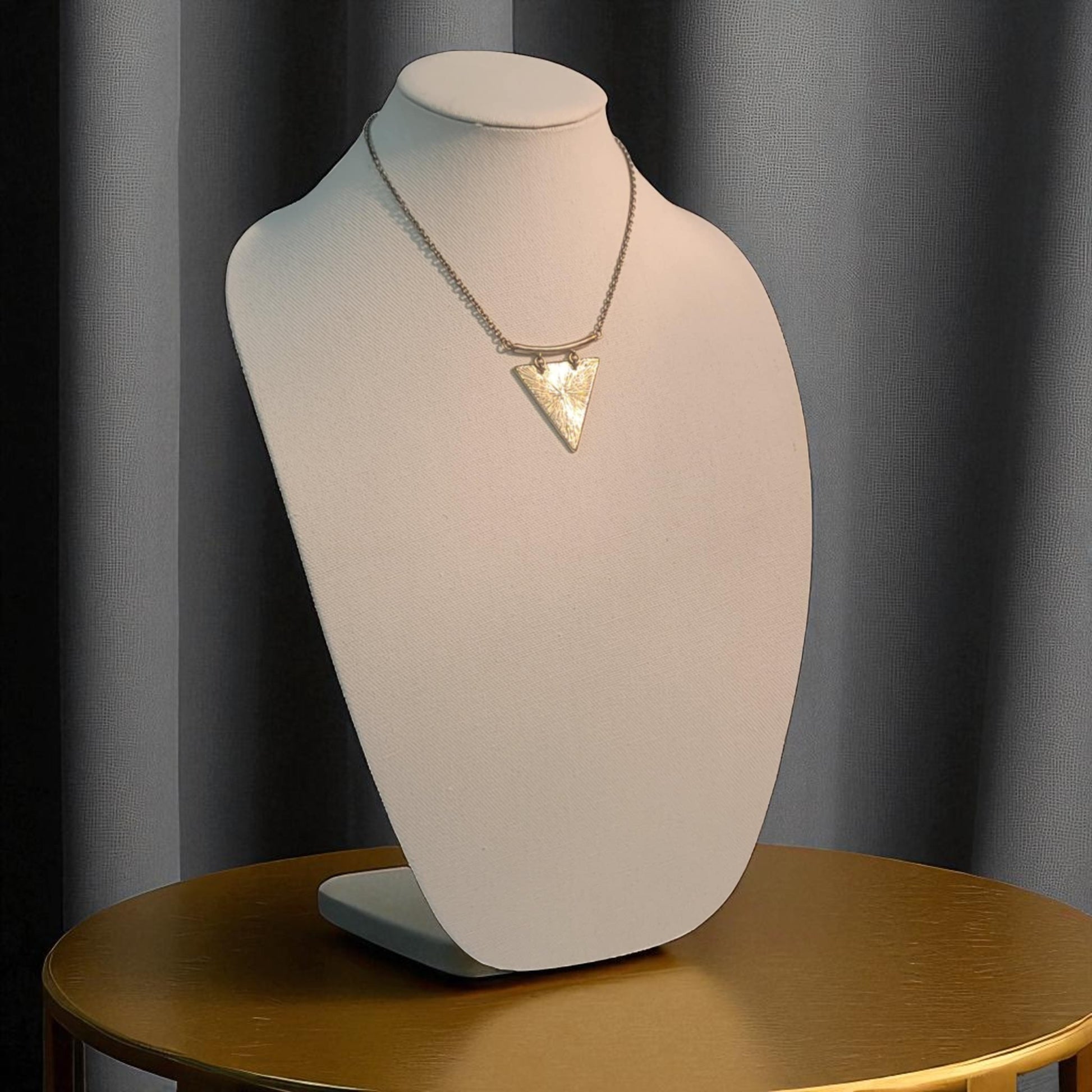 Necklace with a triangle pendant on a mannequin bust against a gray curtain background