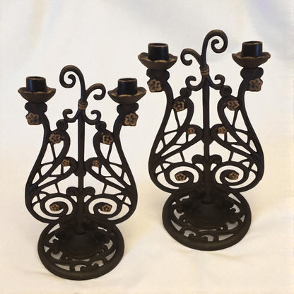 Two black metal candle holders with intricate designs on a white background