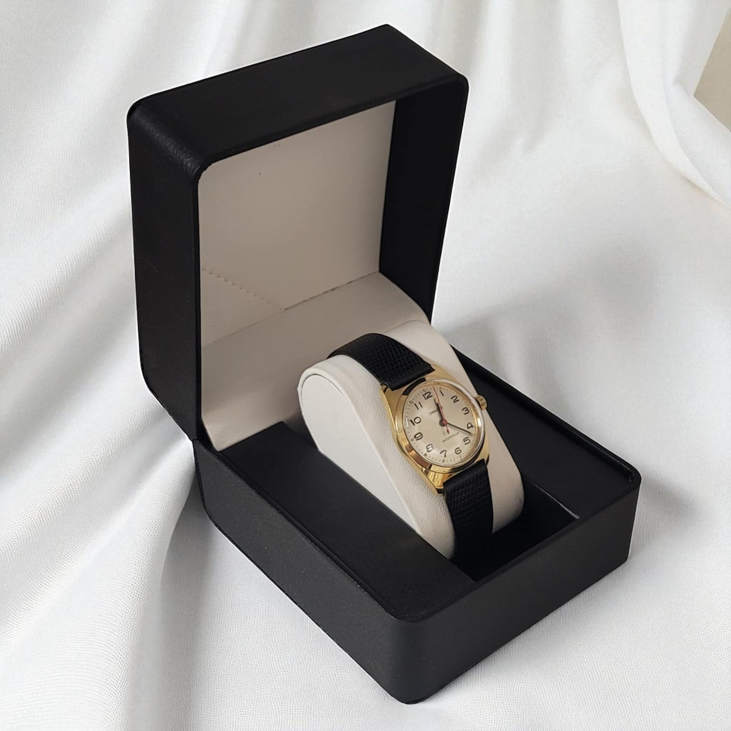 Gold watch with black strap in a black box on a white background