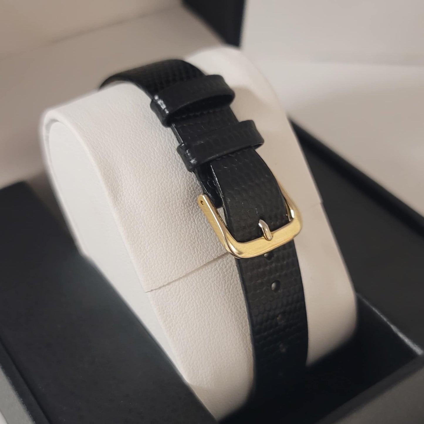 Black leather strap with a gold buckle on a beige cushion