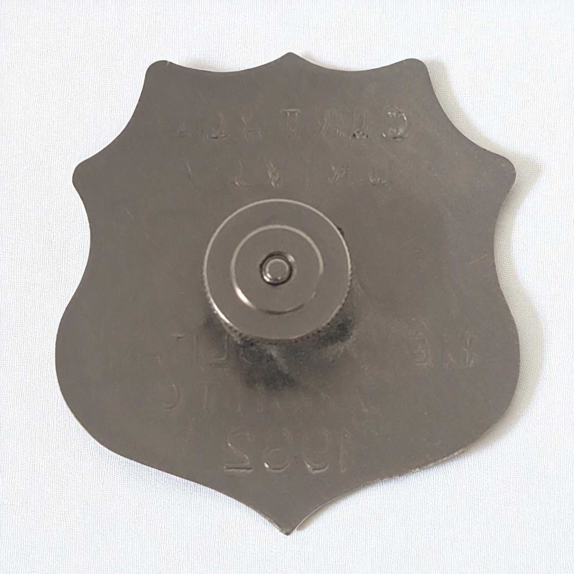 Metal shield-shaped object with central circular component on a white background