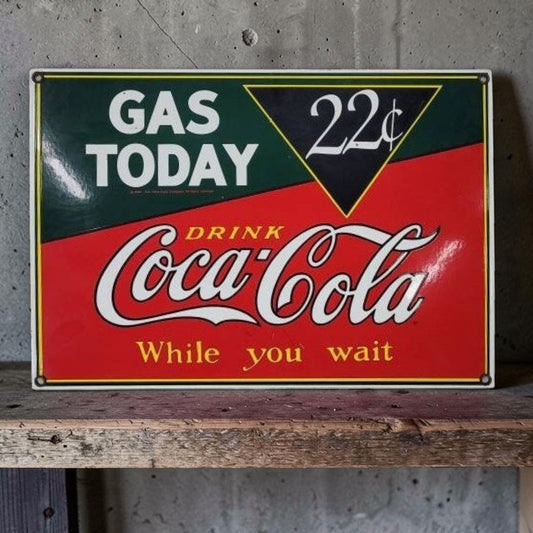 Vintage-style sign advertising gas and Coca-Cola with a concrete wall background