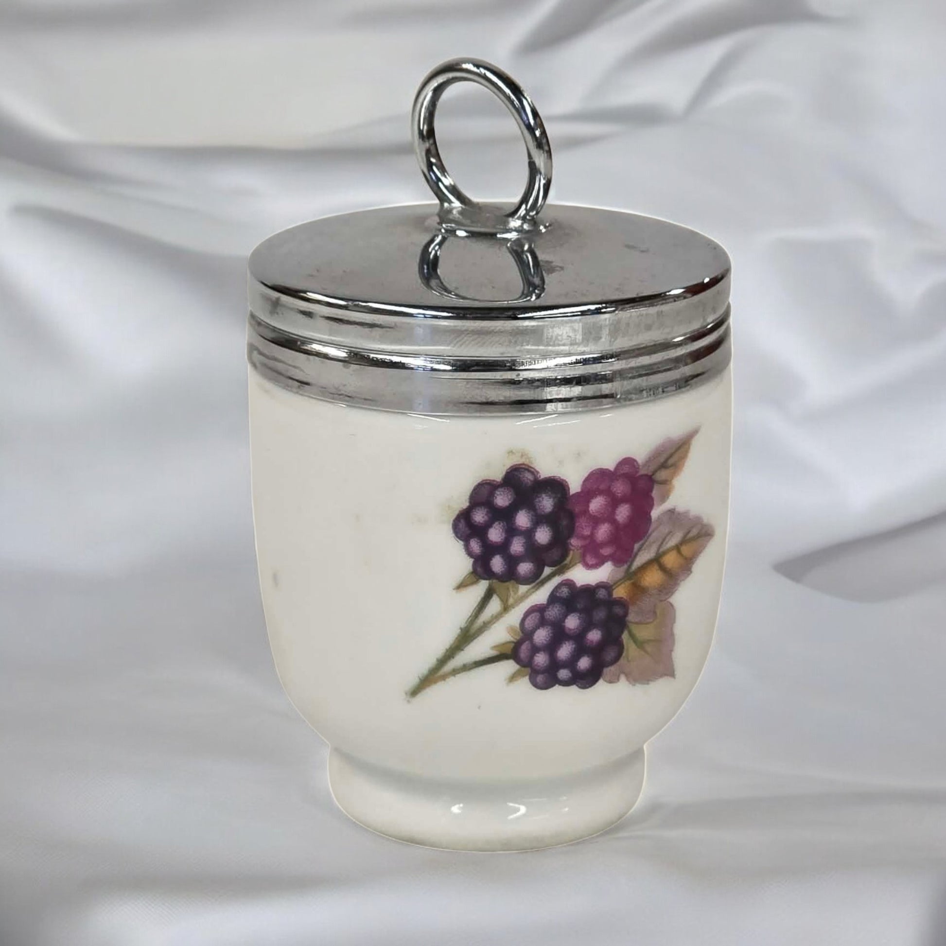 Small ceramic jar with silver lid and blackberry design on a white background
