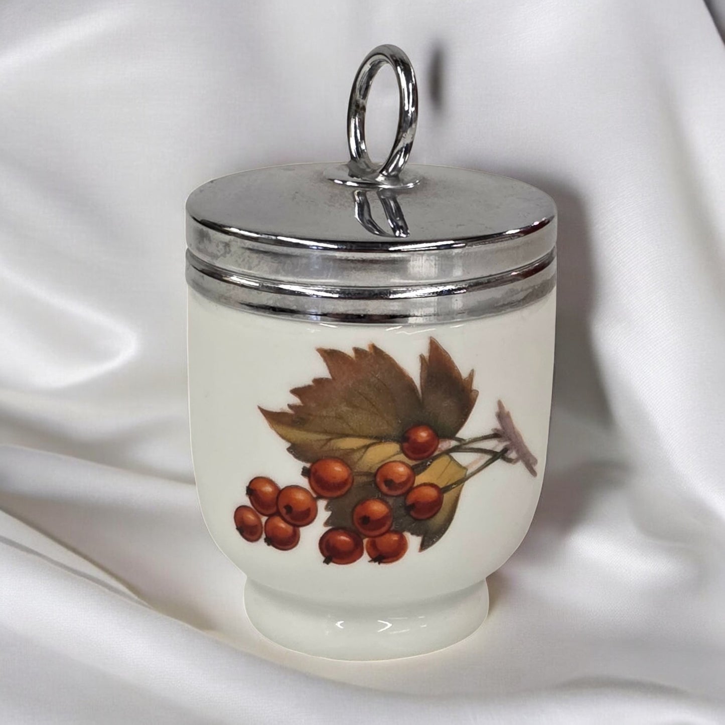 Decorative jar with silver lid and leaf and berry design on a white fabric background