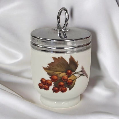 Decorative jar with silver lid and leaf and berry design on a white fabric background