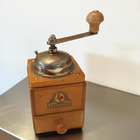 Vintage wooden coffee grinder with brass components on a reflective surface.