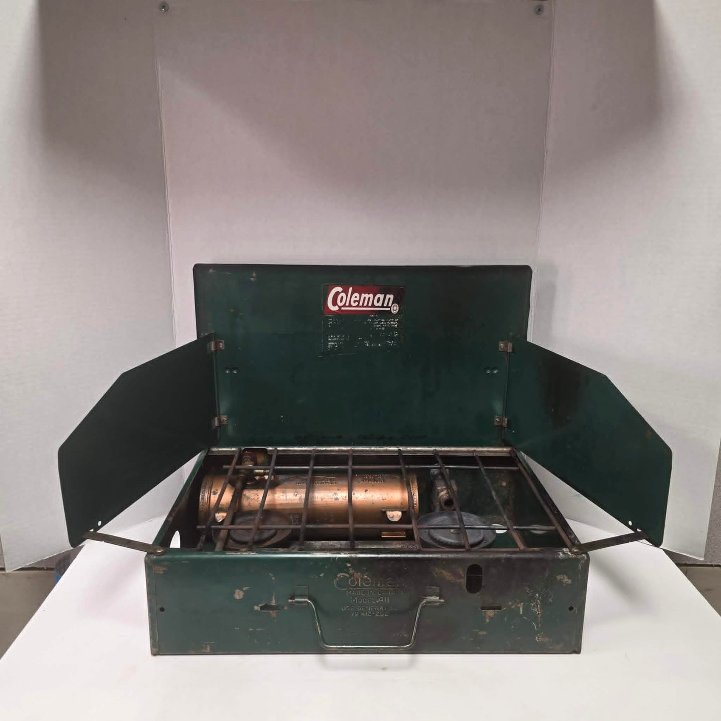 Vintage Coleman Model 411 Canadian suitcase camp stove with copper-colored fuel tank.
