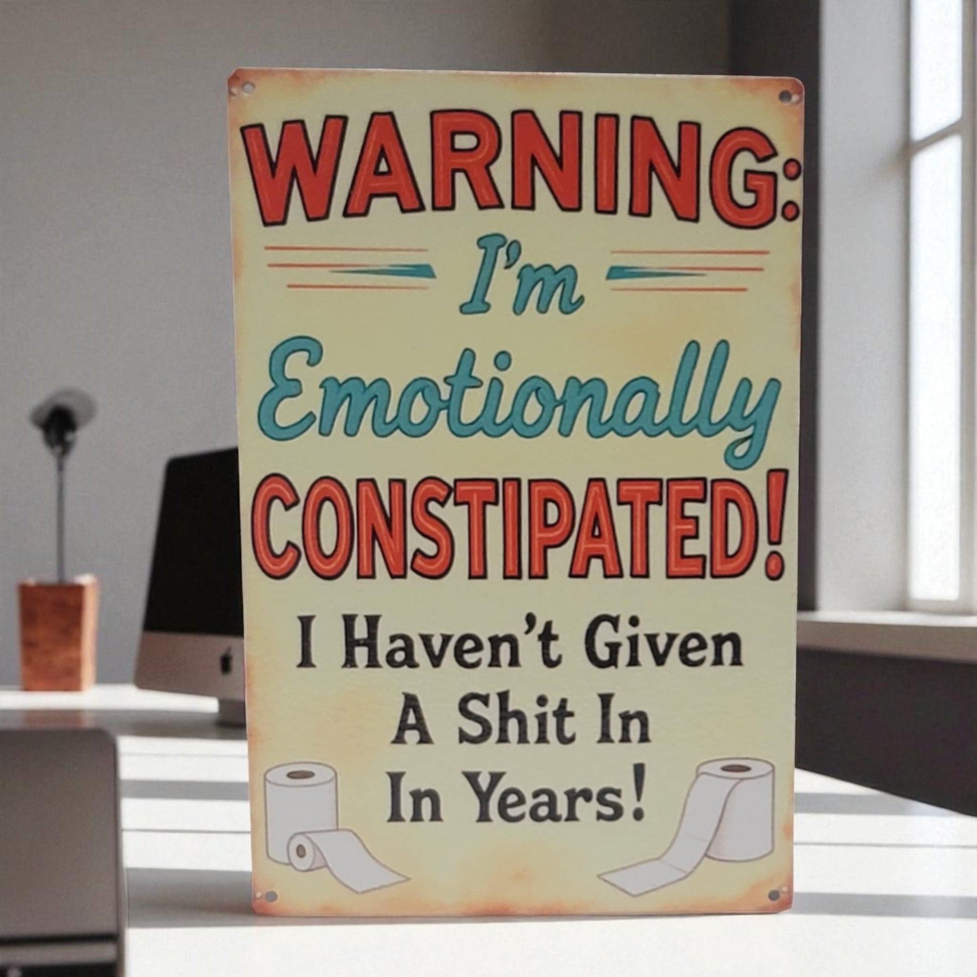 Metal sign with humorous text and graphics on a desk