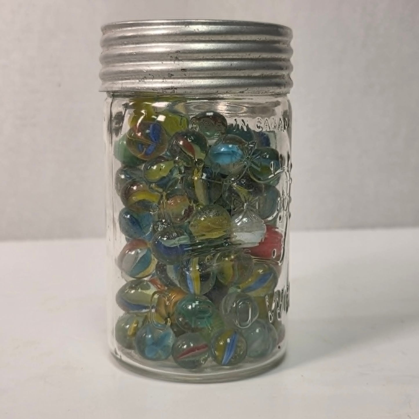 Clear glass jar filled with multicolored marbles on a white background
