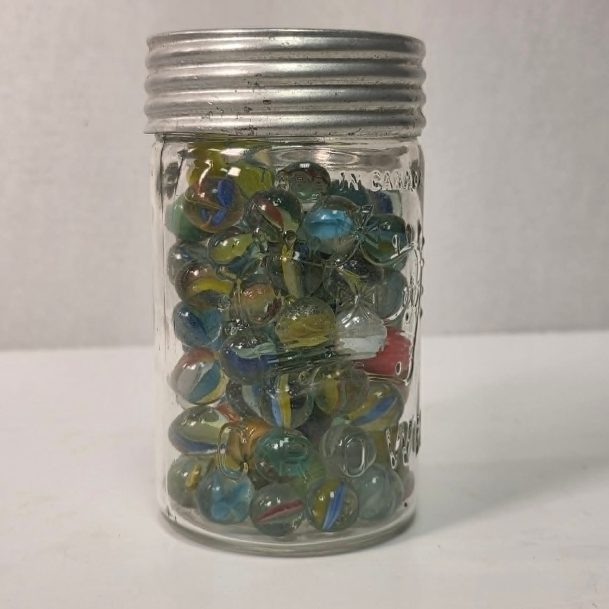Clear glass jar filled with multicolored marbles on a white background