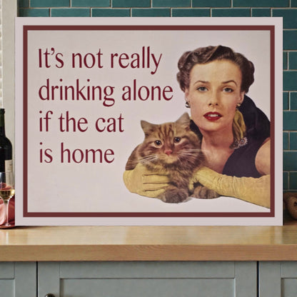 Poster with a woman holding a cat and text 'It's not really drinking alone if the cat is home' on a kitchen counter.