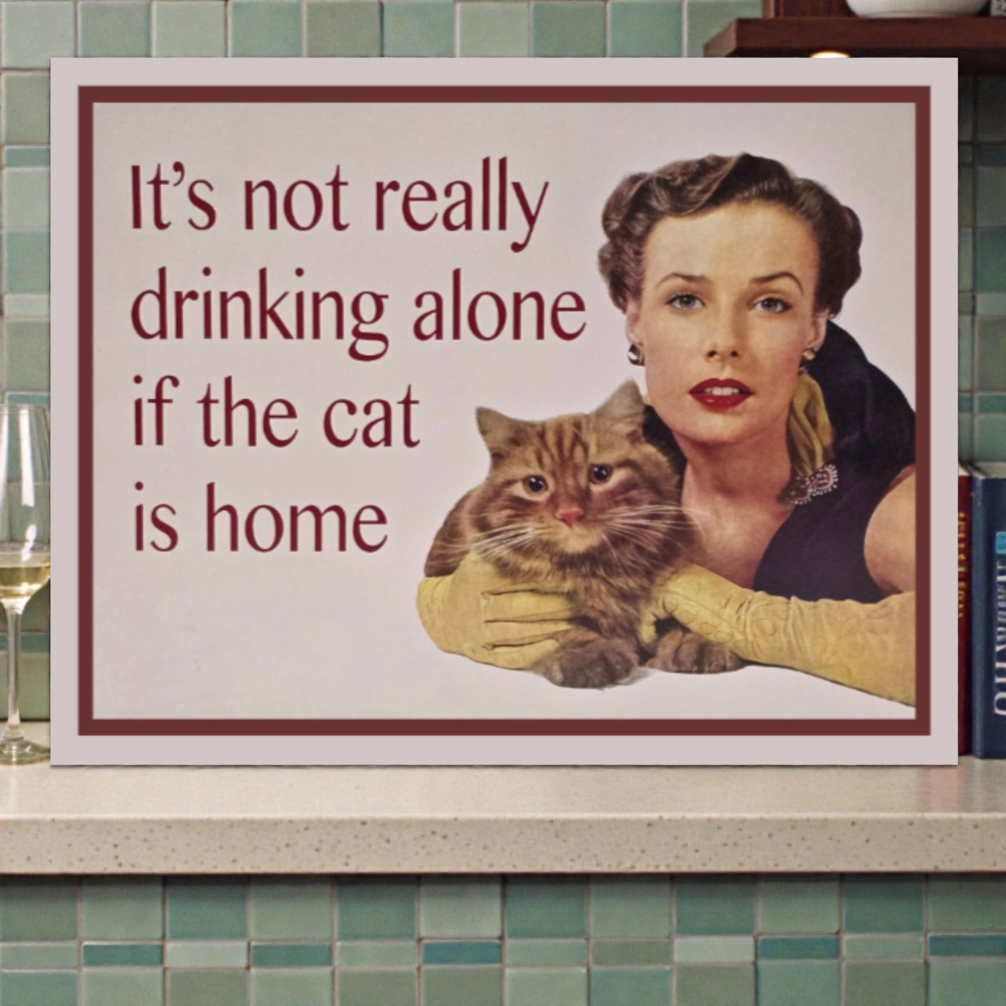 Framed poster with a woman holding a cat and text 'It's not really drinking alone if the cat is home' on a tiled wall.