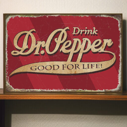 Vintage-style Dr. Pepper sign with red background and gold text on a wooden shelf.