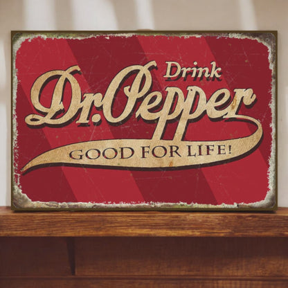 Vintage-style Dr. Pepper sign with red background and gold text on a wooden surface.
