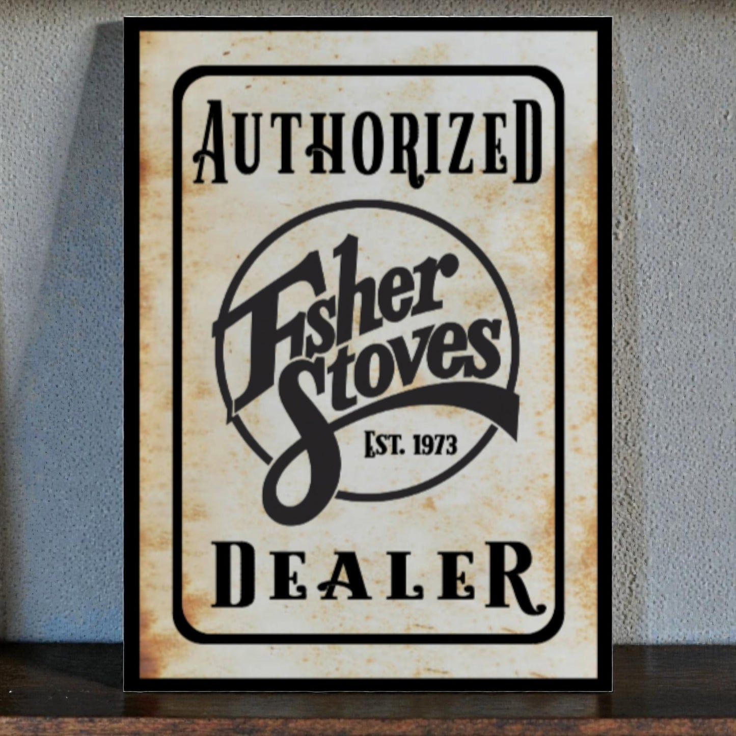 Framed sign for Fisher Stoves Authorized Dealer on a textured wall.