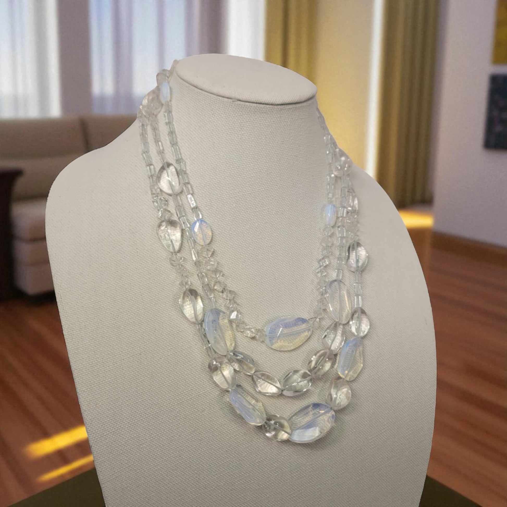 Necklace on a mannequin bust in a room with a couch and curtains.