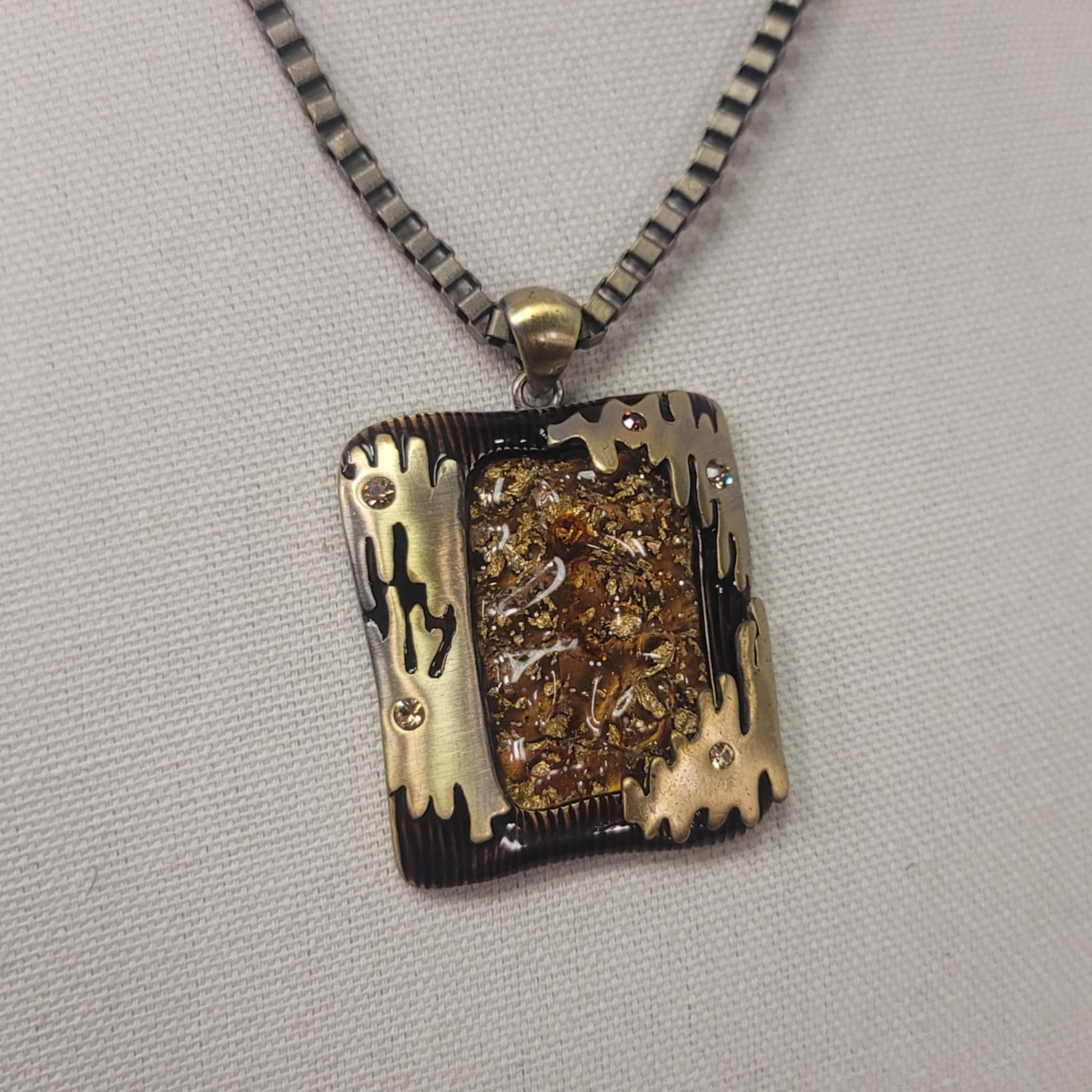 Necklace with a rectangular pendant featuring gold and black designs on a gray background