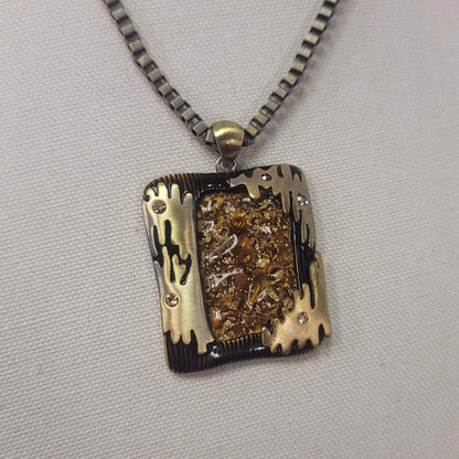 Necklace with a rectangular pendant featuring gold and black designs on a gray background