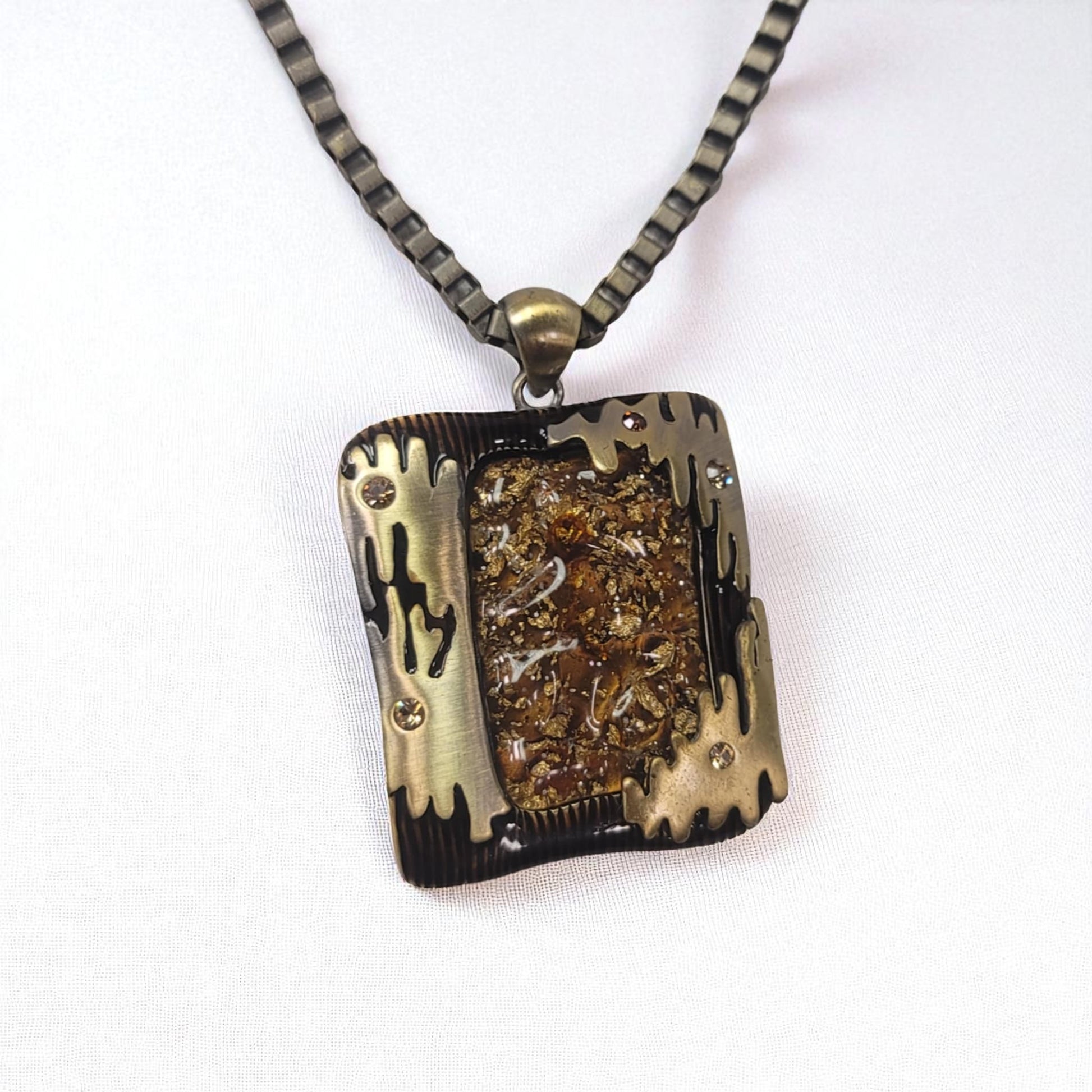Necklace with a rectangular pendant featuring gold and black design on a white background