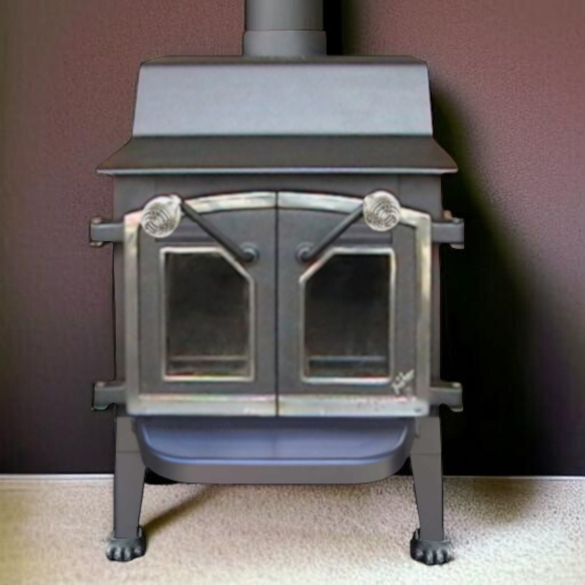 Gray wood stove with glass doors on a beige floor against a dark brown wall.