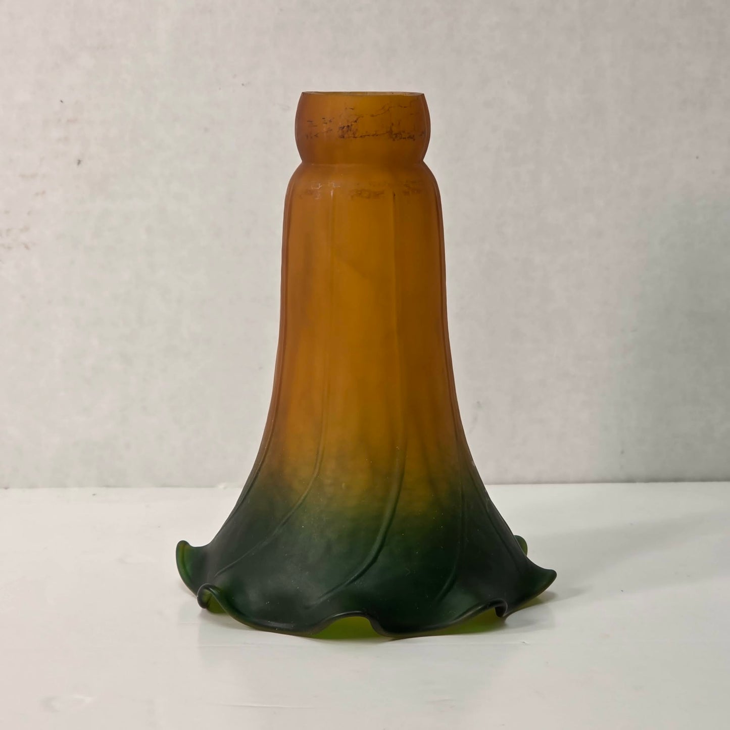 Green and amber tulip-shaped glass lampshade with ruffled edge and mottled interior glow.