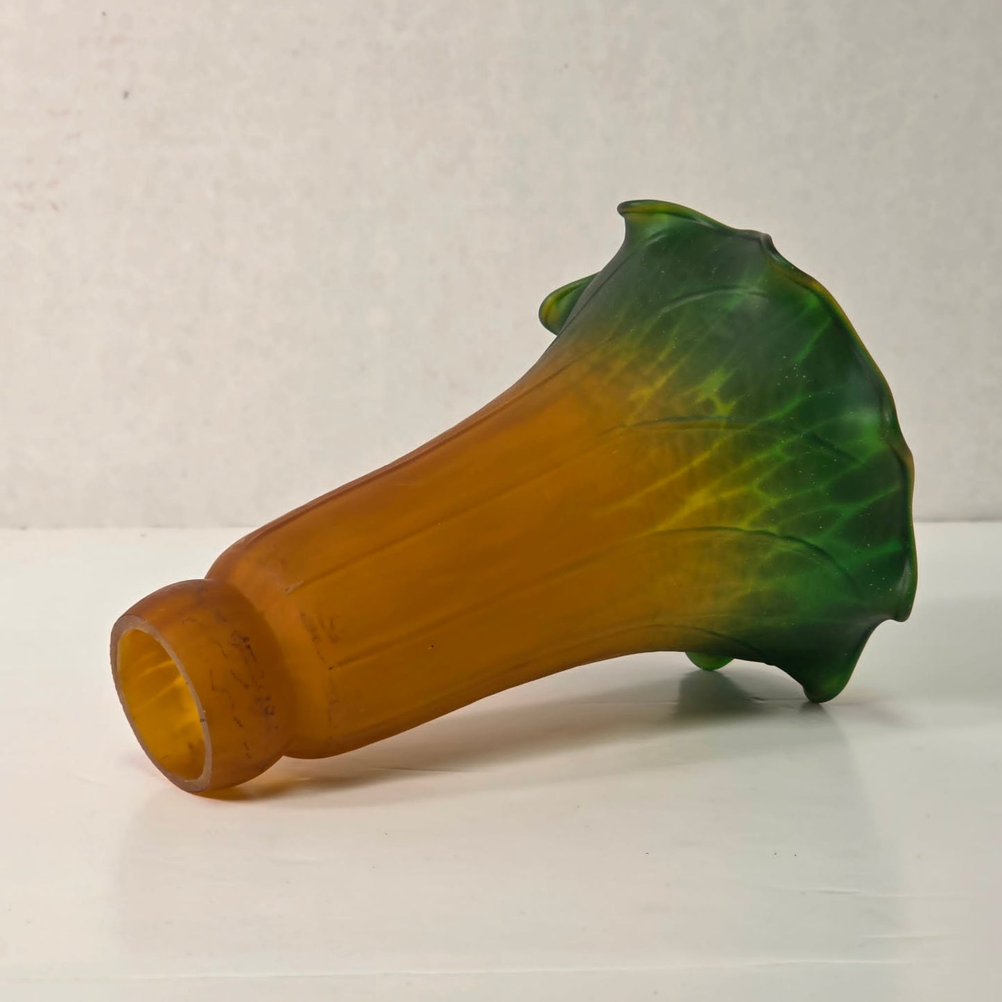Green and amber tulip-shaped glass lampshade with ruffled edge and mottled interior glow.