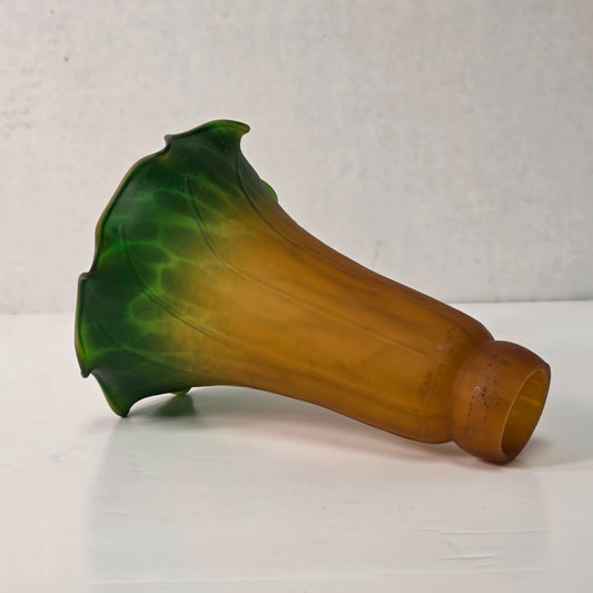Green and amber tulip-shaped glass lampshade with ruffled edge and mottled interior glow.