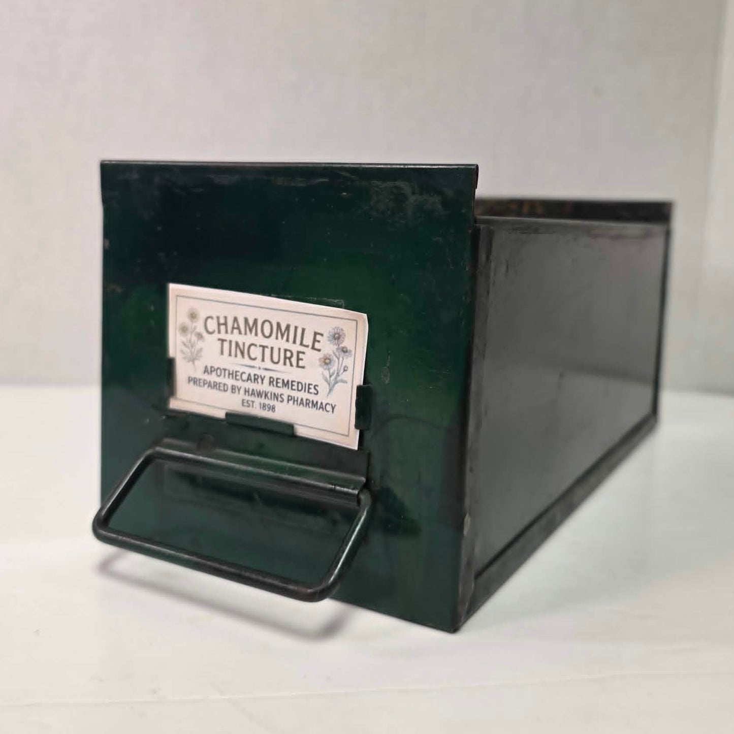 Antique industrial apothecary drawer with bail handle and label holder, vintage storage bin with aged patina.