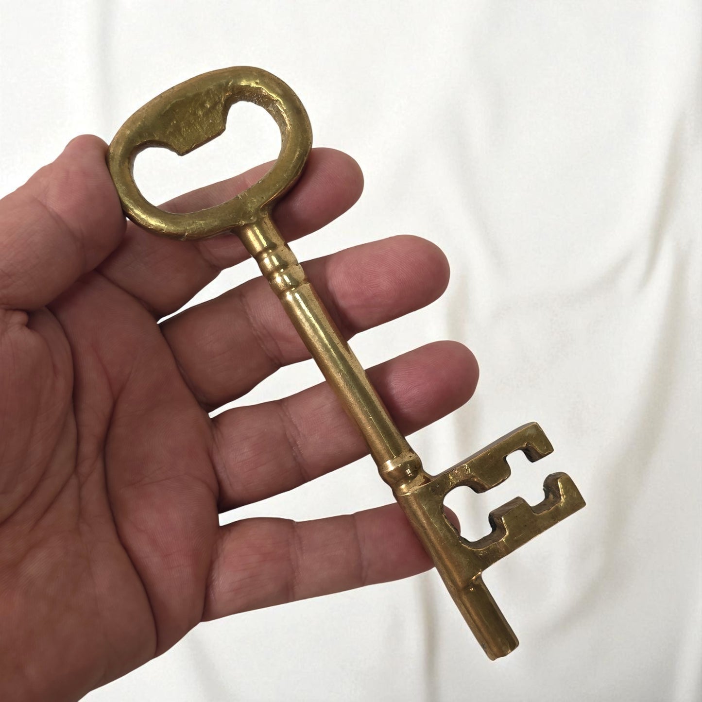 Hand holding a large brass key against a white background
