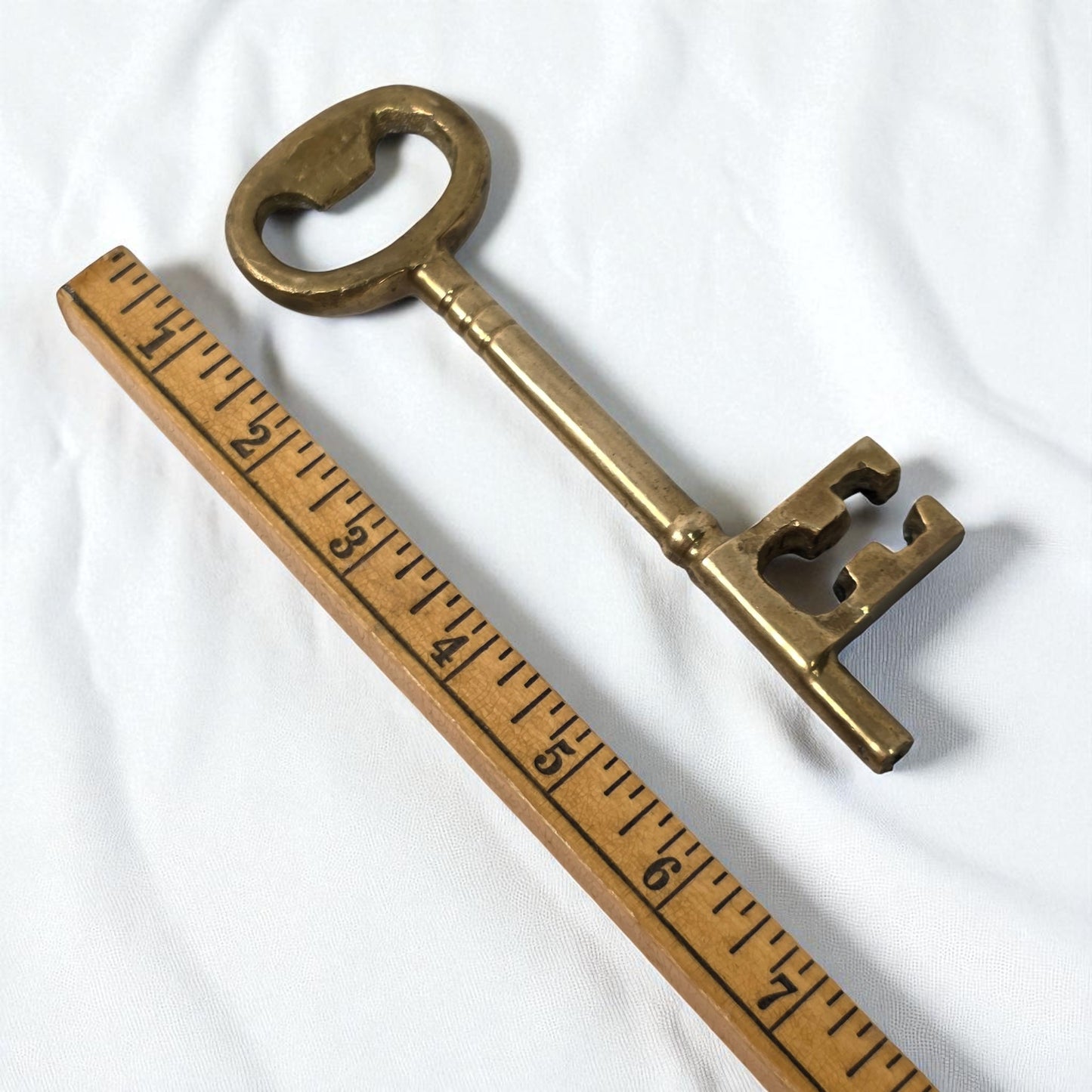 Brass key next to a wooden ruler on a white background