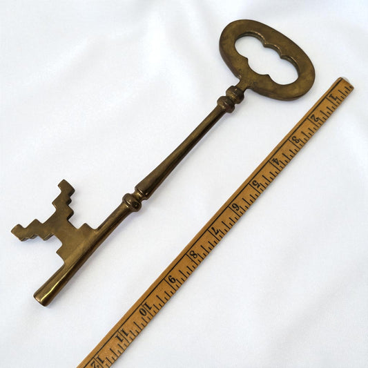 Large decorative brass key next to a ruler on a white background