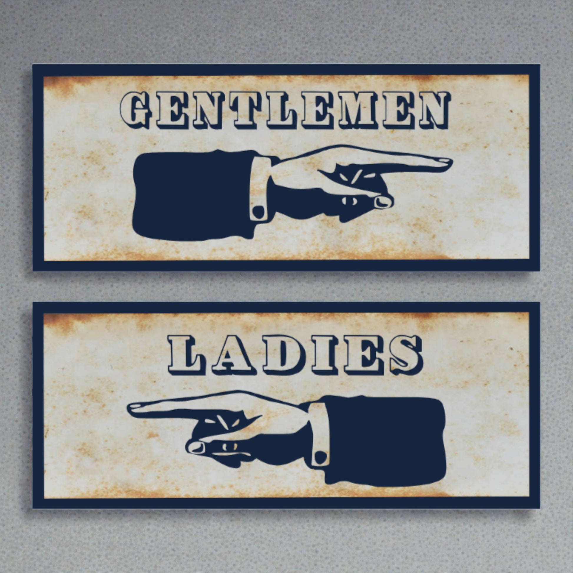 Two restroom signs with pointing hands, one labeled 'Gentlemen' and the other 'Ladies', on a textured surface.