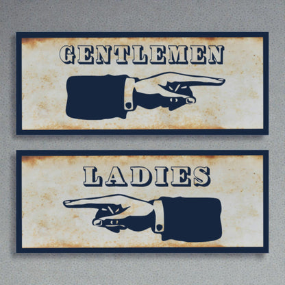 Two restroom signs with pointing hands, one labeled 'Gentlemen' and the other 'Ladies', on a textured surface.
