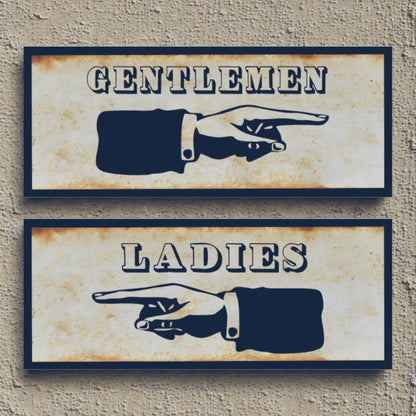 Two vintage-style restroom signs with pointing hands, one for gentlemen and one for ladies, on a textured wall background.