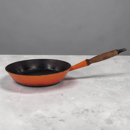 Vintage Le Creuset No. 28 Flame Orange cast iron frying pan with wooden handle.
