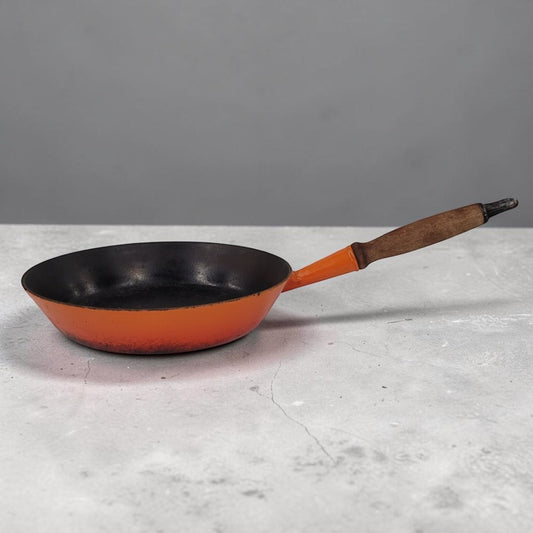 Vintage Le Creuset No. 28 Flame Orange cast iron frying pan with wooden handle.
