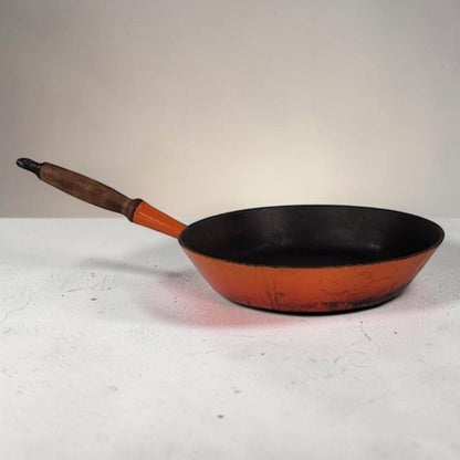 Vintage Le Creuset No. 28 Flame Orange cast iron frying pan with wooden handle.
